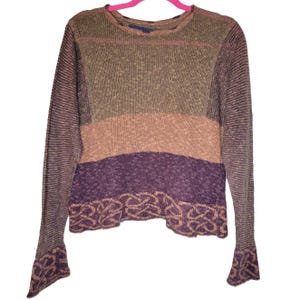 May include: A striped long-sleeved sweater with a brown, pink, and purple color scheme. The sweater has a unique design with a braided pattern at the bottom.