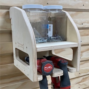 May include: A wall-mounted wooden storage organizer with two clear plastic jars filled with screws and two drill drivers with red and black handles. The drill drivers are labeled "FUEL BRUSHLESS".