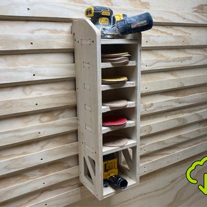 Op de afbeelding: Een houten wandgemonteerde opbergrek met zes planken voor het opbergen van schuurpapier. Een gele en zwarte elektrische schuurmachine bevindt zich op de bovenste plank.