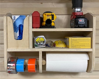 Puede incluir: Un organizador de pared de madera con estantes para herramientas y suministros. Cuenta con un rollo de toallas de papel, un dispensador de guantes y un espacio para rollos de cinta. El organizador tiene una cinta métrica Stanley Powerlock amarilla de 8 m/26', una lijadora amarilla y negra, un taladro rojo y negro y gafas de seguridad amarillas y negras.