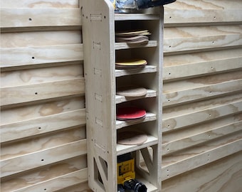 Puede incluir: Un estante de almacenamiento de pared de madera con seis estantes para guardar discos de lijado. Una lijadora eléctrica amarilla y negra cuelga del estante inferior.