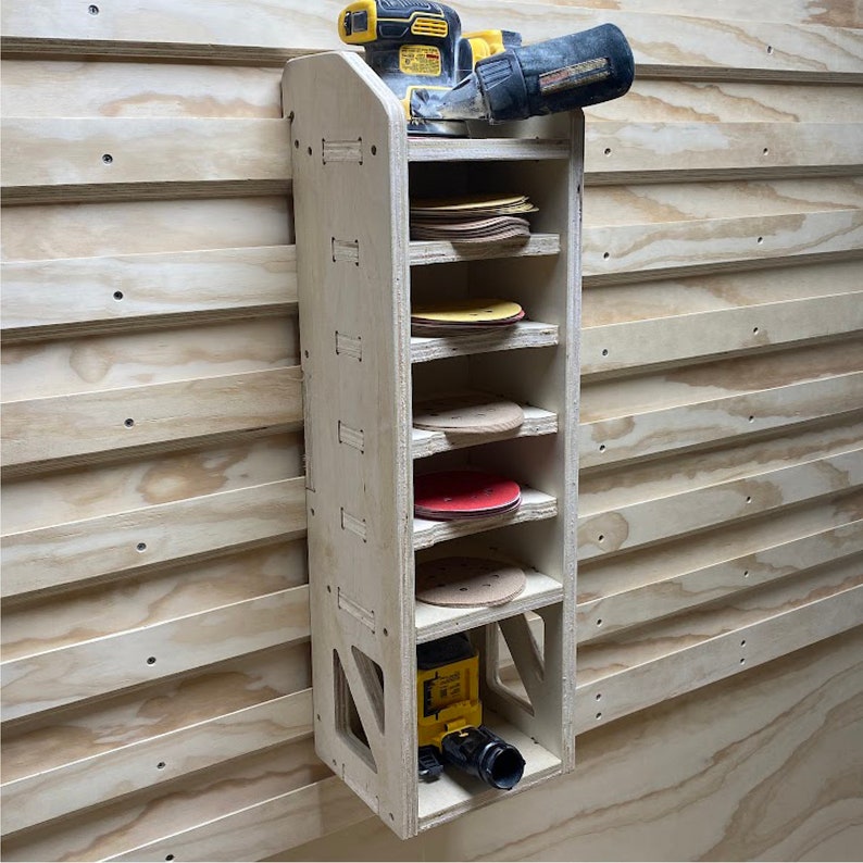Op de afbeelding: Een houten wandrek met zes planken voor het opbergen van schuurpapier. Een gele en zwarte elektrische schuurmachine hangt aan de onderste plank.