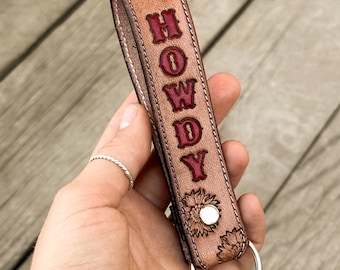 May include: A brown leather keychain with a sunflower design and the word "HOWDY" embossed in red.