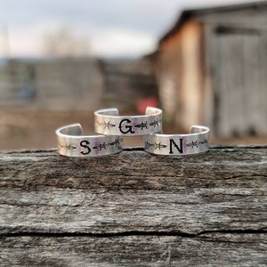 May include: Three silver rings with barbed wire designs and the letters "S", "G", and "N" engraved on them.