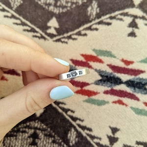 May include: A silver ring with the word "MOM" and a paw print engraved on it.
