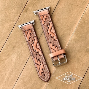 May include: Two light brown leather watch bands with a geometric design. The bands have silver-colored connectors and buckles. The bands are lying on a wooden surface. The Wall Leather Co. logo is visible.