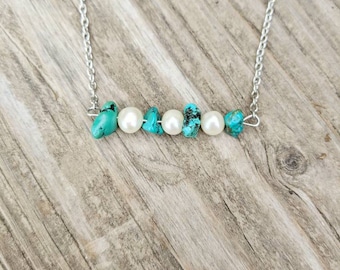 Op de afbeelding: Een zilveren ketting met turquoise en witte parels. De ketting ligt op een houten oppervlak.