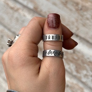 May include: Two silver rings with a geometric pattern of black triangles. The rings are worn on a finger.