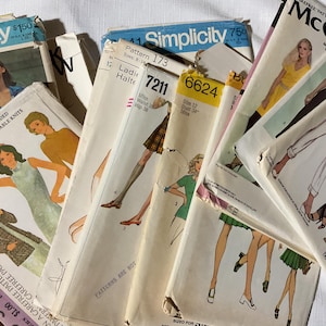 May include: A stack of vintage sewing patterns featuring a variety of designs and colours. The patterns are for clothing and include instructions and diagrams. The patterns are from Simplicity and McCall's brands.