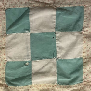 Może przedstawiać: Kołdra patchworkowa z szachownicowym wzorem z białych i turkusowych kwadratów. Kołdra ma różowo-biały kwiatowy brzeg.