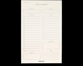 May include: A beige daily planner with a minimalist design. The planner includes sections for gratitude, top goals, schedule, to-do list, self-care, meals, and exercise. The text "DAILY PLANNER" and "simple self" are printed on the page.