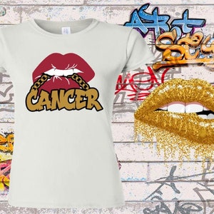 May include: White t-shirt with a red lip design with gold chain and the word "Cancer" in gold letters.