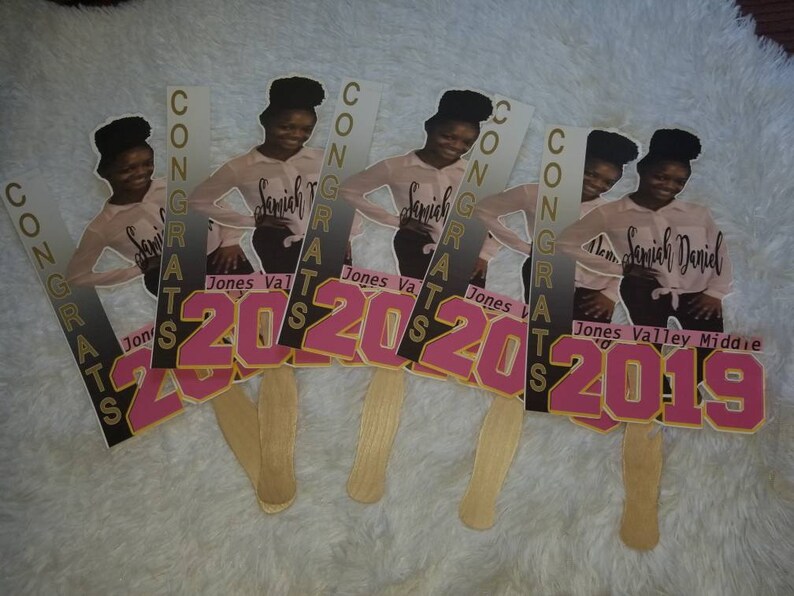May include: Five graduation fan decorations with a photo of a young person in a pink shirt and black pants. The fans have the words "CONGRATS" and the years "2020" and "2019" printed on them.