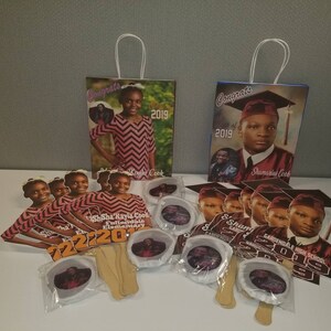 May include: Graduation party favors featuring a red and black color scheme. The favors include paper fans, paper bags, and round paper favors with photos of the graduates. The text "Congrats" and "Class of 2019" are visible on the bags. The text "Sha'Sha Kayla Cook Fultondale Elementary" and "Shamarius Cook Gardendale High School" are visible on the fans.