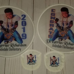 May include: Two white round fan patches with a photo of a young boy wearing a football uniform and holding a football. The text "CONGRATS 2019" is on the left side of the patch and the text "De'Karrius Richardson Avondale Elementary" is on the bottom of the patch.
