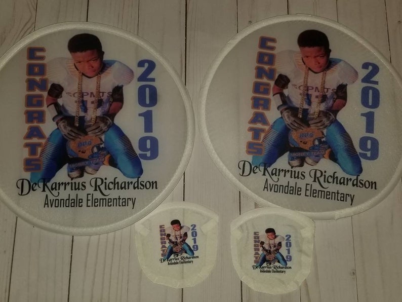 May include: Two white round fan patches with a photo of a young boy wearing a football uniform and holding a football. The text "CONGRATS 2019" is on the left side of the patch and the text "De'Karrius Richardson Avondale Elementary" is on the bottom of the patch.