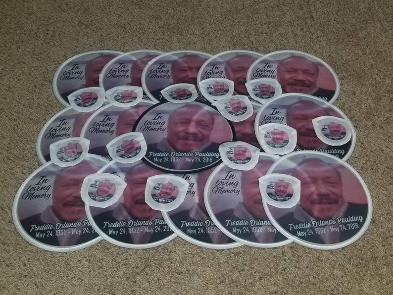 May include: A stack of white paper fans with a black border and a photo of a man. The fans have the text "In loving memory" and "Freddie Orlando Paulding" with dates of birth and death.