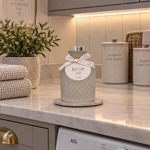 Puede incluir: Una botella de vidrio esmerilado con textura de rombos, que presenta un tapón plateado y una cinta blanca atada al cuello. Una etiqueta redonda blanca unida a la cinta muestra el texto LUSSO Gifts y las palabras Posh Hemp en negro.