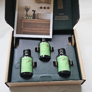 Könnte beinhalten: Eine offene Pappschachtel mit drei kleinen schwarzen Flaschen Purdy & Figg Lime & Lemongrass Bathroom Bliss. Eine kleine Karte mit einer Badeszene und Anweisungen ist sichtbar.
