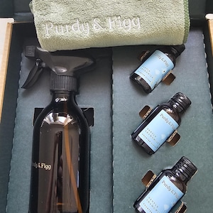 Könnte beinhalten: Ein Reinigungsset bestehend aus einer dunklen Braunglas-Sprühflasche mit schwarzem Sprühkopf, drei kleinen Braunglasflaschen mit hellblauen Etiketten der Marke Purdy & Figg Gentle Chamomile Counter Clean und einem salbeigrünen Mikrofasertuch.