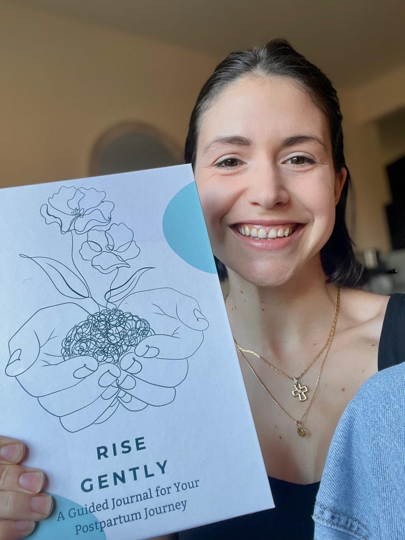 Op de afbeelding: Een wit tijdschrift met de woorden "RISE GENTLY" en "A Guided Journal for Your Postpartum Journey" op de omslag. De omslag toont een lijntekening van handen die een plant met bloemen en een lichtblauwe cirkel omarmen.