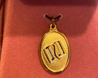 May include: A gold oval pendant with a design of two open books. The pendant is on a black cord and is in a red velvet box.