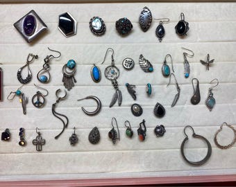 Peut inclure: Une collection de bijoux argentés assortis comprenant diverses boucles d'oreilles, pendentifs et broches. Les pièces présentent des pierres précieuses variées comme la turquoise, l'améthyste et l'onyx, ainsi que des breloques en métal en forme de plumes, de croix et de cercles.