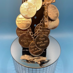 May include: Gold charm bracelet with a crucifix and round charms featuring the Ten Commandments. The charms are engraved with the text "Thou shalt not..." and "Remember thou keep holy the Sabbath day".