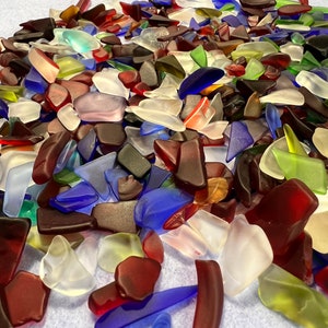 May include: A large pile of colorful sea glass pieces in various shapes and sizes. The glass is mostly clear, blue, green, and red.