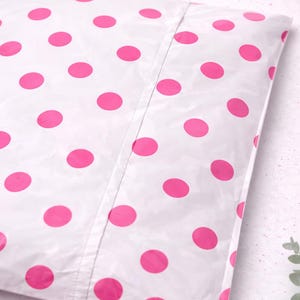 May include: White poly mailer with a pattern of large, evenly spaced, bright pink polka dots. The mailer is sealed with a seam down the center. The background is a light, speckled surface.