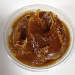 Puede incluir: Primer plano de una sustancia marr&oacute;n, espesa y cremosa en un recipiente de pl&aacute;stico transparente.