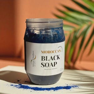 Puede incluir: Un tarro transparente lleno de jab&oacute;n negro marroqu&iacute; azul oscuro. La etiqueta dice "MOROCCAN BLACK SOAP" con la marca "Nature & Traditions". El tarro contiene 250g de jab&oacute;n y est&aacute; hecho con ingredientes 100% naturales. Una peque&ntilde;a cantidad de polvo azul est&aacute; esparcida debajo.