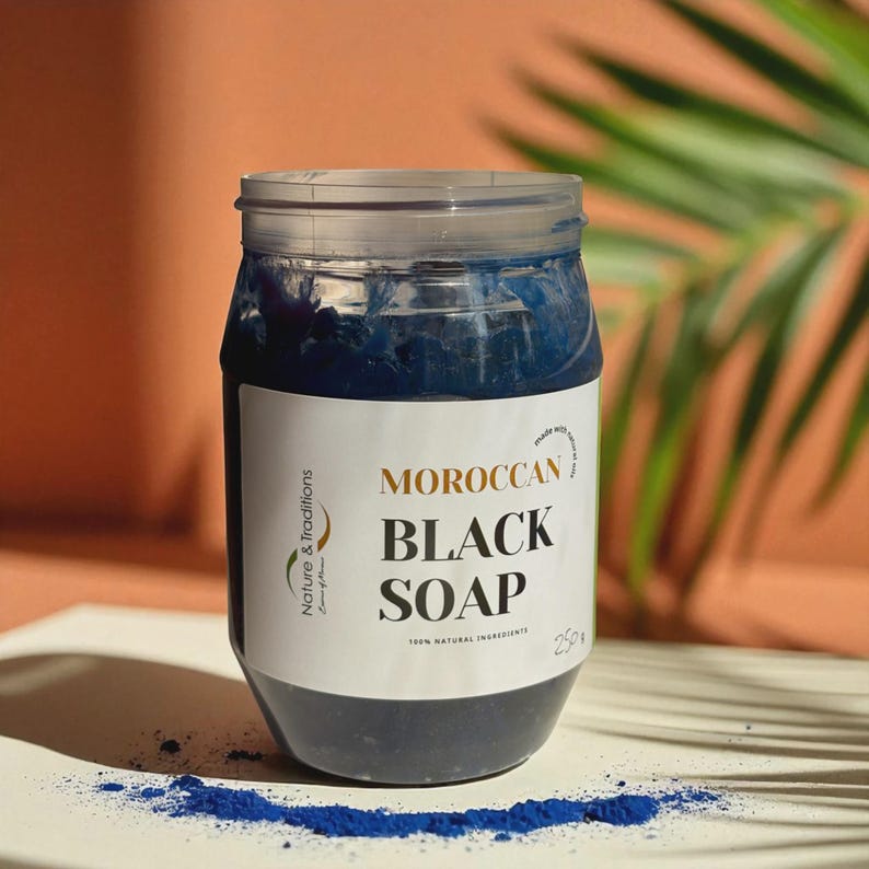 Puede incluir: Un tarro transparente lleno de jab&oacute;n negro marroqu&iacute; azul oscuro. La etiqueta dice "MOROCCAN BLACK SOAP" con la marca "Nature & Traditions". El tarro contiene 250g de jab&oacute;n y est&aacute; hecho con ingredientes 100% naturales. Una peque&ntilde;a cantidad de polvo azul est&aacute; esparcida debajo.