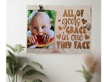 May include: A wooden photo frame with a picture of a baby eating watermelon. The frame has the text "All of god's grace in one tiny face" with hearts around the words.