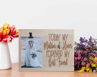 May include: A wooden photo frame with a clip to hold a photo. The frame has the text "TODAY MY MATRON OF HONOR FOREVER MY BEST FRIEND" engraved on it. The photo shows two people in a field.