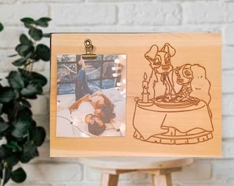 May include: A wooden photo frame with a clip to hold a photo. The frame has a laser-engraved design of two dogs sitting at a table with a candle. The photo in the frame shows a couple lying on a bed.