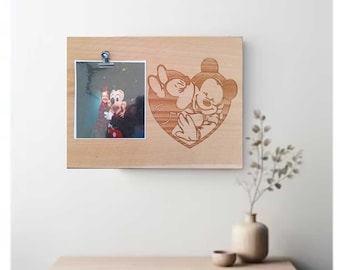 May include: A wooden photo frame with a cutout of Mickey Mouse and Minnie Mouse in a heart shape. A photo of a young girl with Mickey Mouse is displayed in the frame.