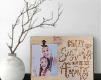 May include: A wooden photo frame with a clip to hold a photo. The frame has the text "Crazy Sisters Make the Best Aunts" engraved on it.