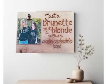 May include: Wooden photo frame with a picture of two women, one blonde and one brunette, held by a clip. The frame has the text "Just a brunette and a blonde with an unbreakable bond" engraved on it.