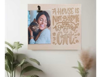 May include: A wooden photo frame with a clip to hold a photo. The frame has the text "A house is not a home without a cat" engraved on it. The photo shows a woman holding a cat.
