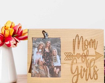 May include: A wooden photo frame with a clip to hold a photo. The frame has the text "Mom of Girls" with an arrow and heart design. The photo shows three people.