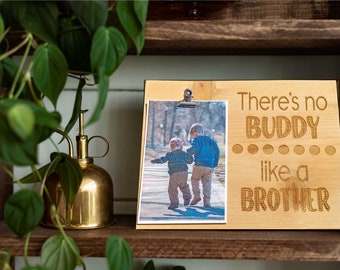 May include: A wooden photo frame with a clip on top. The frame has a photo of two boys walking down a sidewalk. The text "There's no BUDDY like a BROTHER" is engraved on the frame.