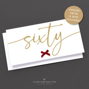 May include: A white greeting card with the word "sixty" in gold script, a small red bow, and the text "CHOOSE FROM 16 BOW COLOURS" on a gold circle. The card is on a dark grey background.