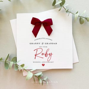 May include: A white card with a burgundy bow and the words "Congratulations Granny & Grandad on your Ruby Wedding Anniversary". The card features a red heart with the number 40.