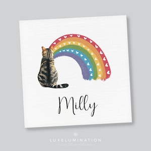 May include: A square print showing a tabby cat gazing at a rainbow adorned with hearts. The name "Milly" is written in cursive below the cat and rainbow. The print is set against a white backdrop.