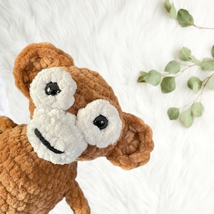 May include: A brown crocheted monkey plush toy with white fur around the eyes and mouth. The monkey has black button eyes.