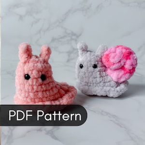 May include: Two crocheted amigurumi snail plushies. One is pink and the other is gray with a pink shell. The image includes the text "PDF Pattern".