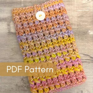 May include: A handmade crochet case in a mix of colors including pink, yellow, orange, and purple. The case has a button closure and the text "PDF Pattern" is displayed on the front. The case is made of yarn and has a textured appearance.