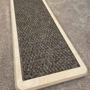 May include: A brown rectangular carpet stair tread with a wooden frame. The carpet is textured and has a light brown border.