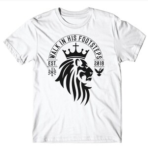 May include: White t-shirt with a black graphic design of a lion's head wearing a crown. The graphic also includes the text "Walk in His Footsteps", "Est. 2018", a cross, and a dove.